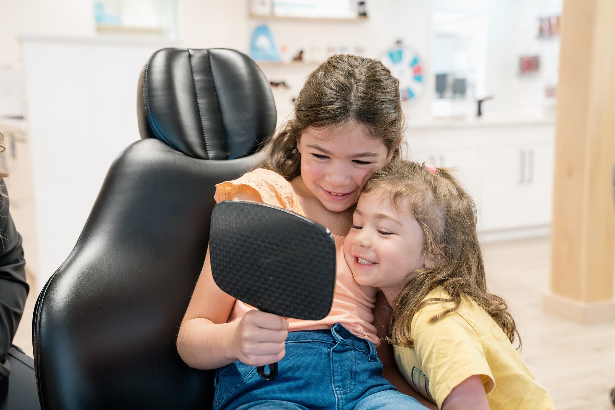 Young patient smiling at her reflection in a hand mirror during an orthodontic visit